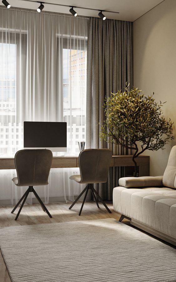 Modern home office setup with two chairs, a desk, computer, large windows, curtains, potted plant, and a cozy sofa.