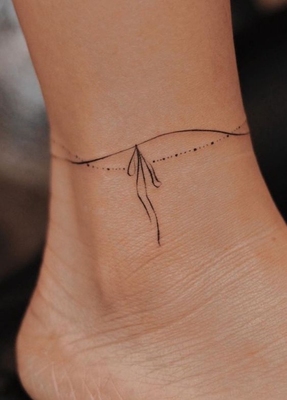 Minimalist fine-line ankle tattoo with a delicate bow design, offering a chic and subtle body art option.