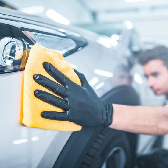 Person polishing car headlight with yellow cloth, wearing black gloves. Car detailing, maintenance, and cleaning.