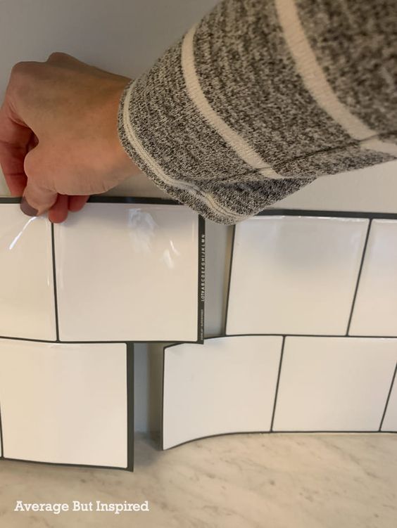 Installing peel-and-stick white subway tile backsplash for a DIY home improvement kitchen project.