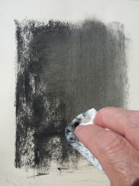 A hand using a cloth to blend charcoal on paper for drawing, demonstrating smoothing and shading techniques in art.