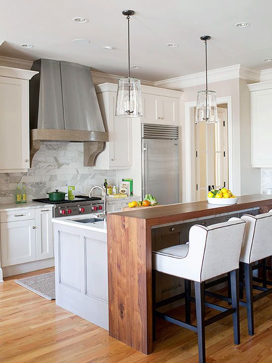 Modern kitchen with stainless steel appliances, wooden island bar, white cabinets, pendant lights, and marble backsplash.