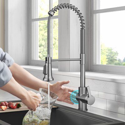 Modern kitchen with stainless steel pull-down faucet, person rinsing a bowl beside strawberries, large windows in background.