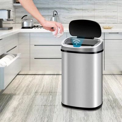 Person using a touchless sensor trash can in a modern kitchen, demonstrating hands-free waste disposal.