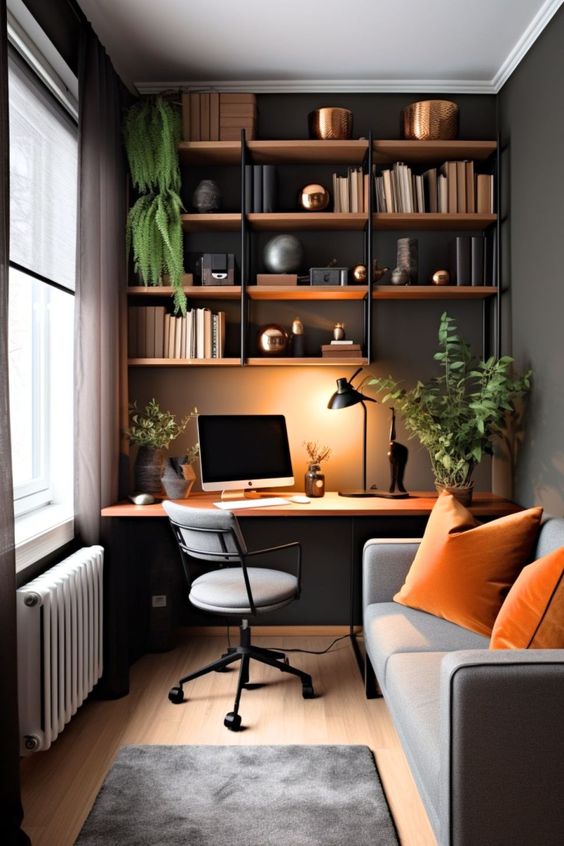 Modern home office with cozy decor, plants, bookshelves, gray sofa, and a wooden desk setup with a computer and lamp.