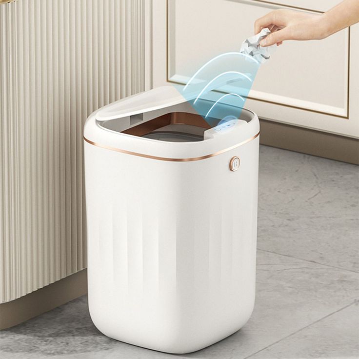 Touchless sensor trash can with lid opening automatically, modern kitchen, hand throwing garbage into sleek white bin.