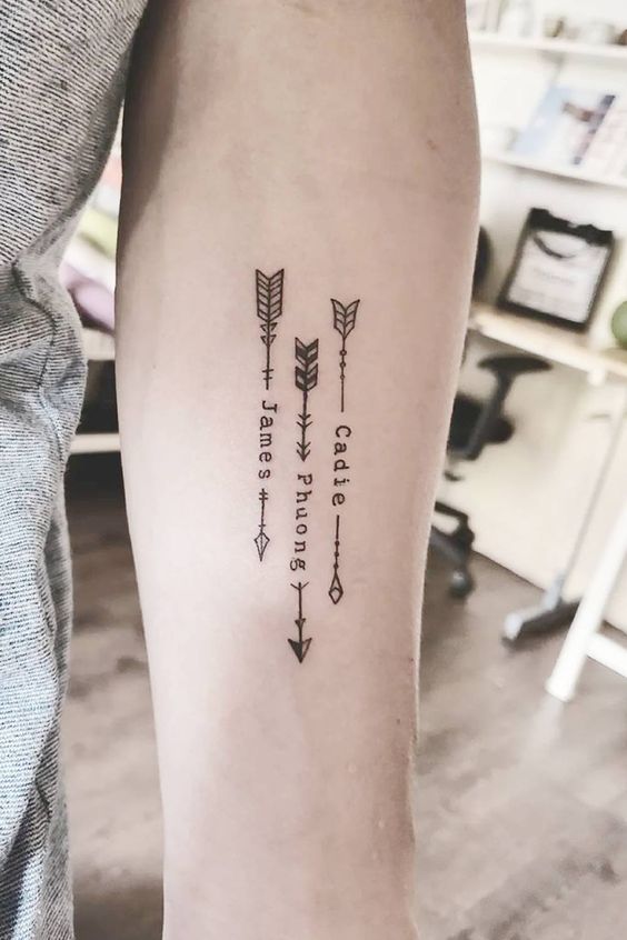 Three minimalist arrow tattoos on an arm with the names James, Phong, and Cadie written vertically along the arrows.
