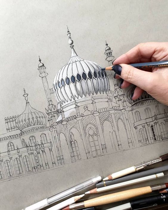 Drawing of a mosque-like building being shaded with pencils by an artist's hand, various drawing tools scattered below.