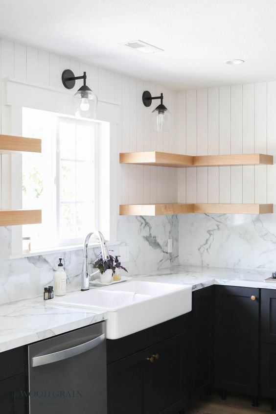 Modern farmhouse kitchen with white marble countertops, wooden floating shelves, black cabinets, and a farmhouse sink.