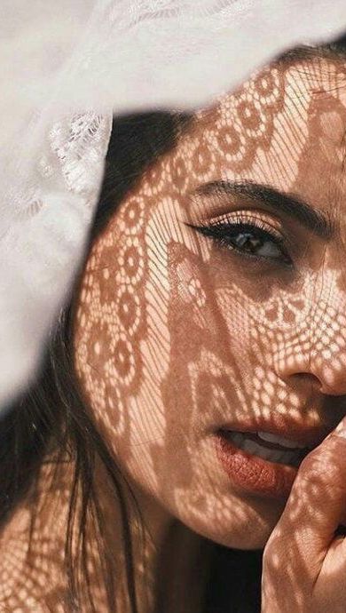 Woman's face with intricate lace shadow pattern on skin, creating a delicate and artistic look. Fashion and beauty concept.