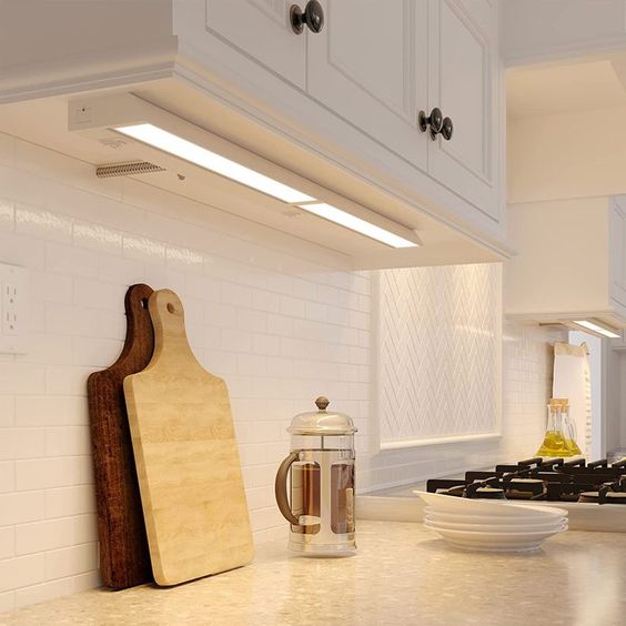 Modern kitchen with under-cabinet lighting, cutting boards, French press coffee maker, and stove. Bright and stylish.