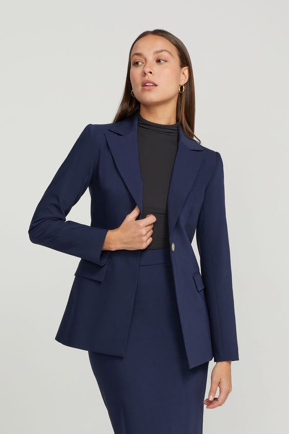 Professional woman in a tailored navy blazer and skirt, posing confidently against a plain background. Business attire.