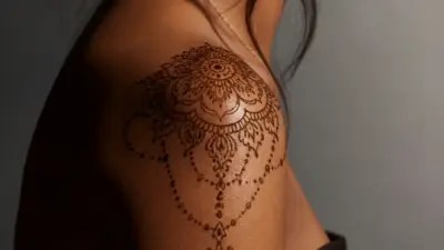 Close-up of ornate mandala henna shoulder tattoo with decorative dot-chain design on woman's tan skin
