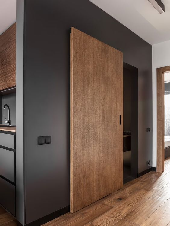 Modern interior with sliding wooden door, black walls, and hardwood floors in a minimalist apartment.