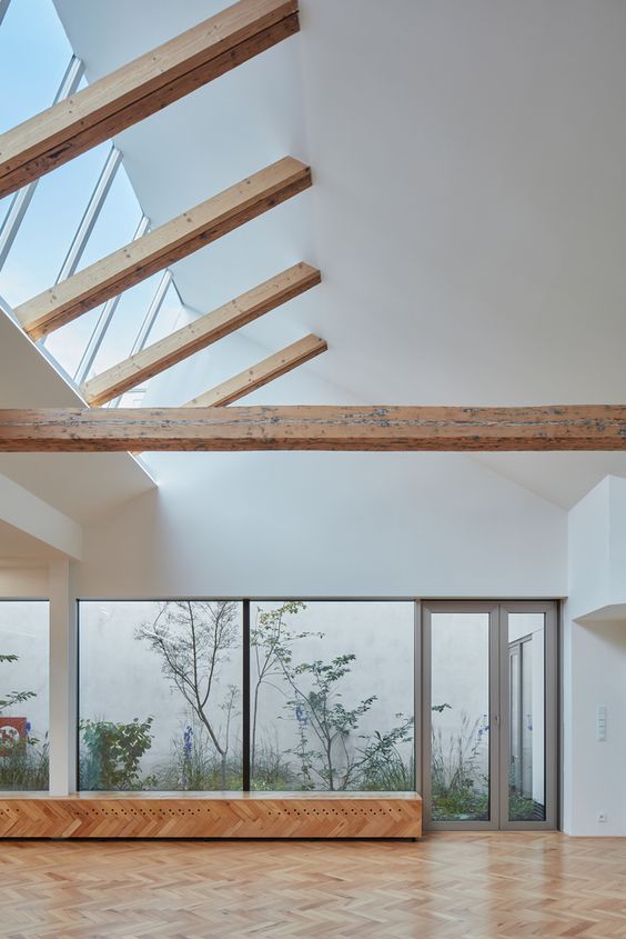 Modern living room with large windows, wooden beams, and parquet flooring, offering natural light and a serene garden view.