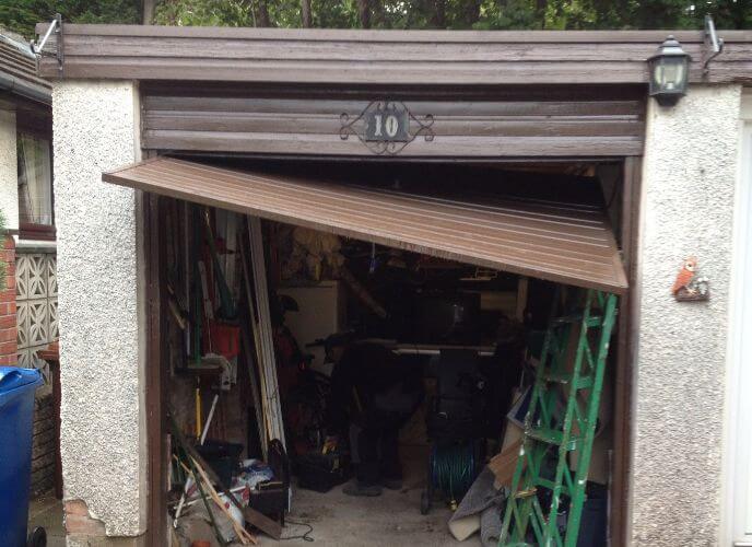 Broken garage door with number 10, partially open, showing cluttered interior with tools and equipment.