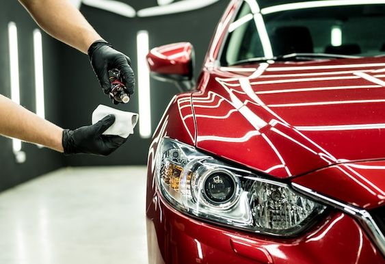 Detailing a red car: hand applying ceramic coating to vehicle's hood for a shiny, protected finish in a professional auto workshop.