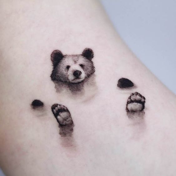 Realistic bear tattoo design on skin, featuring the bear’s head and paws in detailed black and gray shading.