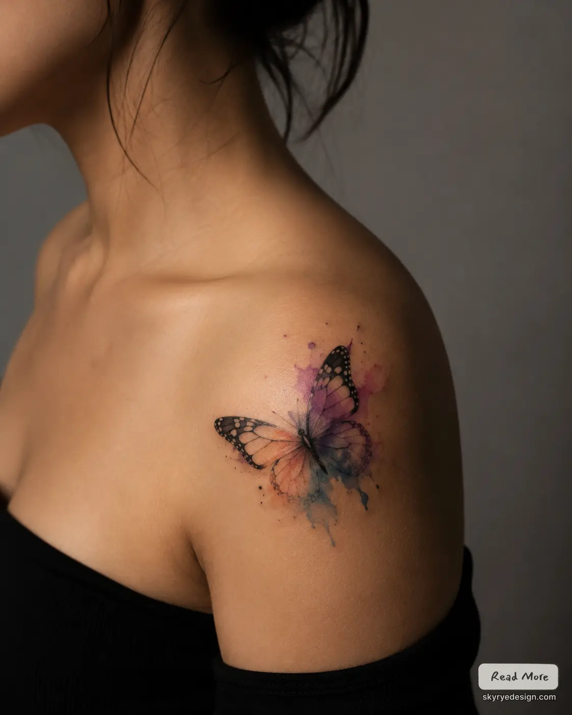 Watercolor butterfly shoulder tattoo with purple, orange and blue splashes on woman's upper shoulder
