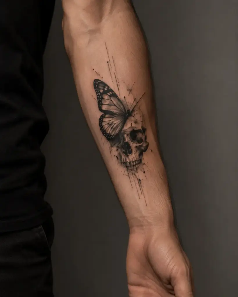 Forearm black-and-gray tattoo of a skull merging with a monarch butterfly, detailed linework and splatter shading.