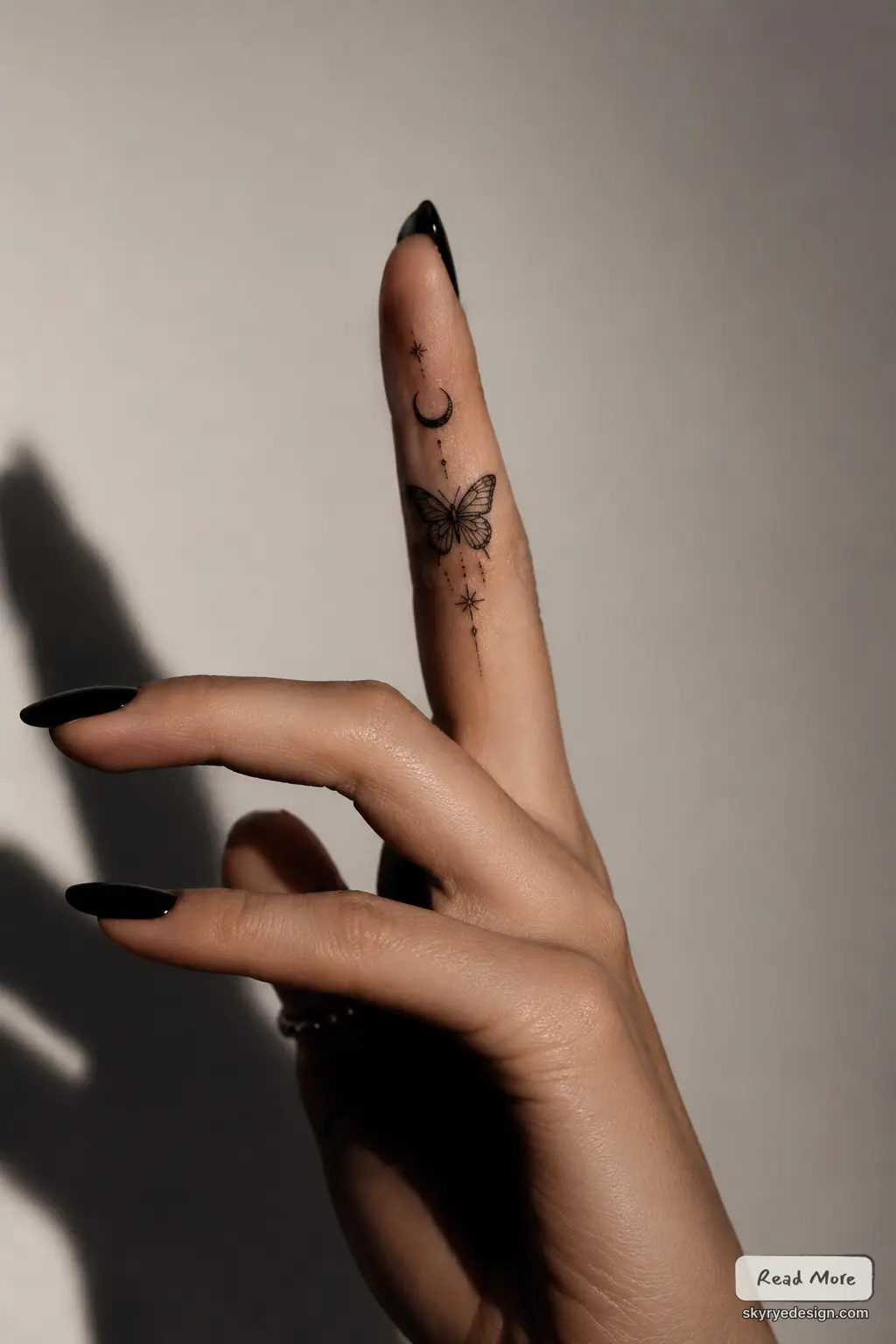Minimalist finger tattoo: butterfly, crescent moon & stars on hand with black stiletto nails, close-up