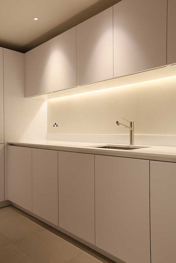 Minimalist modern kitchen with sleek white cabinets, under-cabinet lighting, and stainless steel sink and faucet.