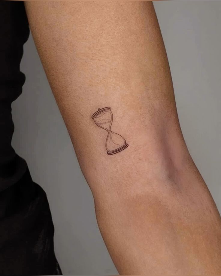 Minimalist hourglass tattoo on inner forearm symbolizing time and life. Small, clean, black line art design.