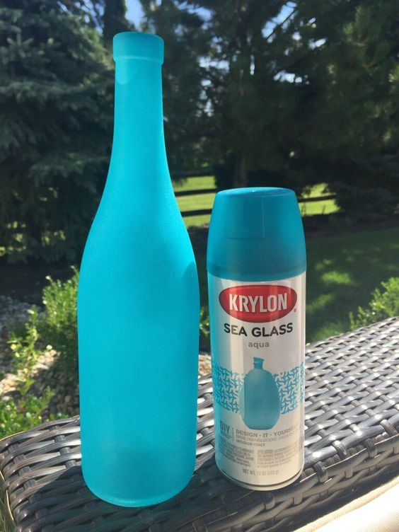 Bright blue bottle next to Krylon Sea Glass Aqua spray paint can on outdoor wicker table basking in sunlight.