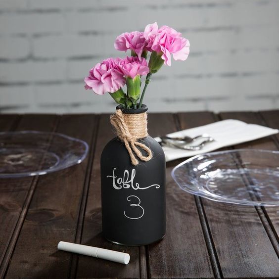 Table centerpiece with pink flowers in a vase labeled table 3 on wooden surface with glass plates in the background.