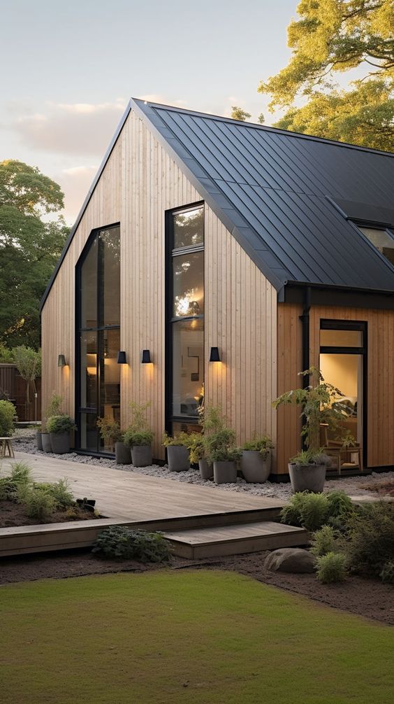 Modern wooden house with large windows, black metal roof, and garden, set in a serene outdoor setting with greenery.