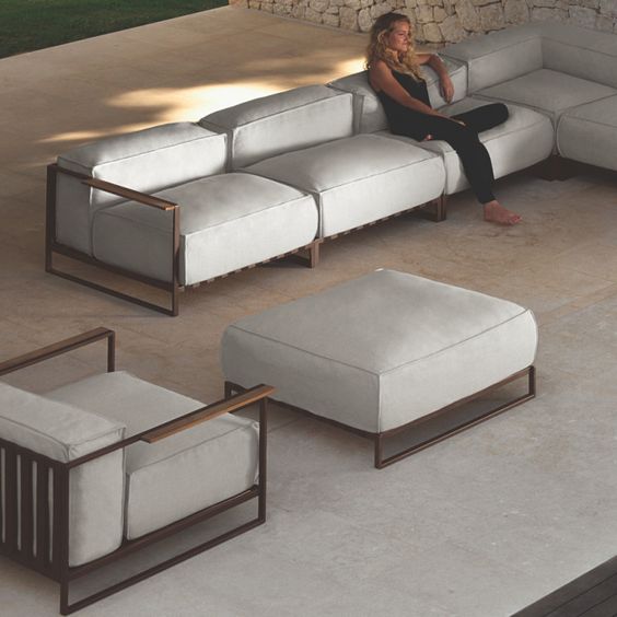 Modern outdoor patio furniture set with white cushions and a woman relaxing on a sectional sofa.