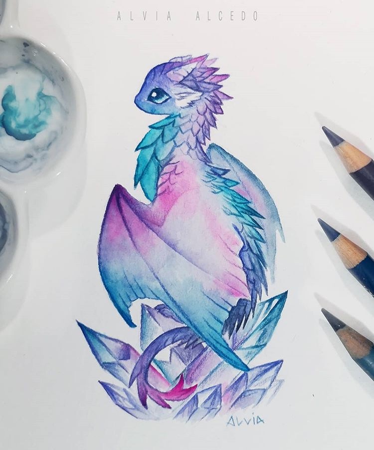 Watercolor painting of a colorful baby dragon surrounded by crystals, with paint palette and pencils nearby.