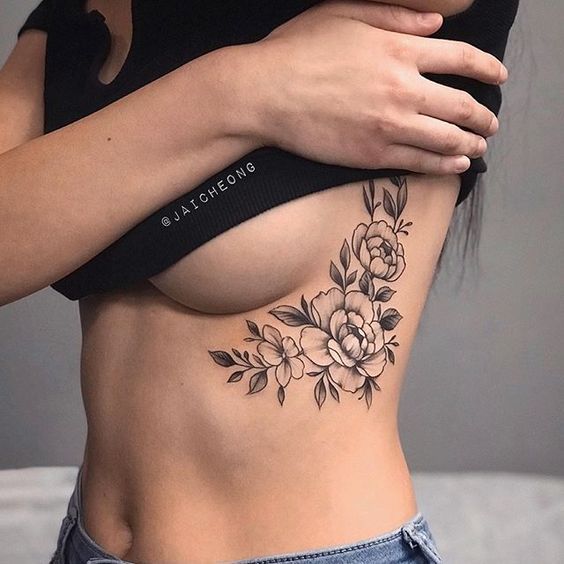 Side rib floral tattoo design showcasing detailed blooming flowers and leaves under a black crop top.