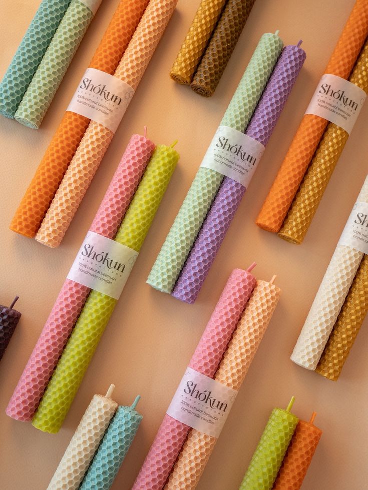 Colorful rolled beeswax candles arranged in pairs on a flat surface, featuring Shokun brand labels.