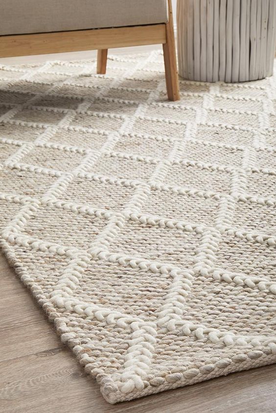 Textured white area rug with geometric pattern under beige sofa and white side table on wooden floor.