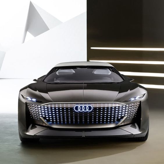 Futuristic Audi concept car with illuminated grille, sleek design, and LED headlights in a modern showroom.