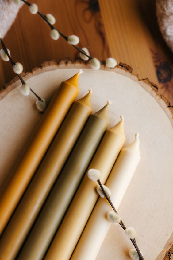 Colorful taper candles laid on wooden surface with pussy willow branches, creating a rustic, cozy atmosphere.