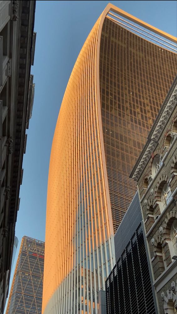 Modern skyscraper with unique curved design in a cityscape, reflecting sunlight, surrounded by other tall buildings.