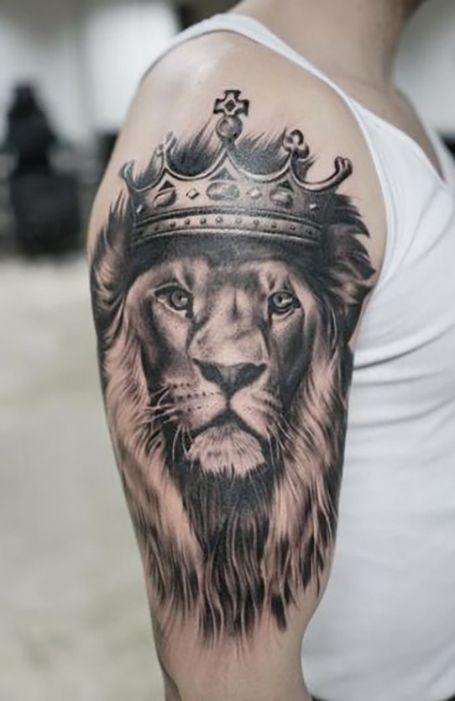 Lion tattoo with a crown on the upper arm of a person wearing a white tank top.