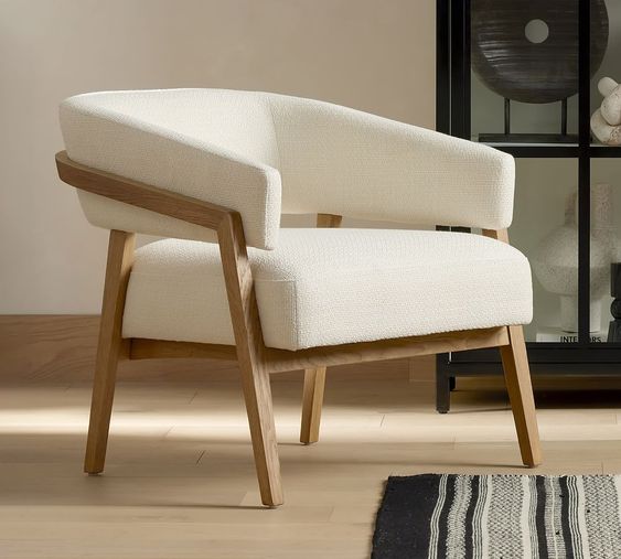 Modern white armchair with wooden legs in a minimalist living room setting, featuring a rug and black cabinet in the background.