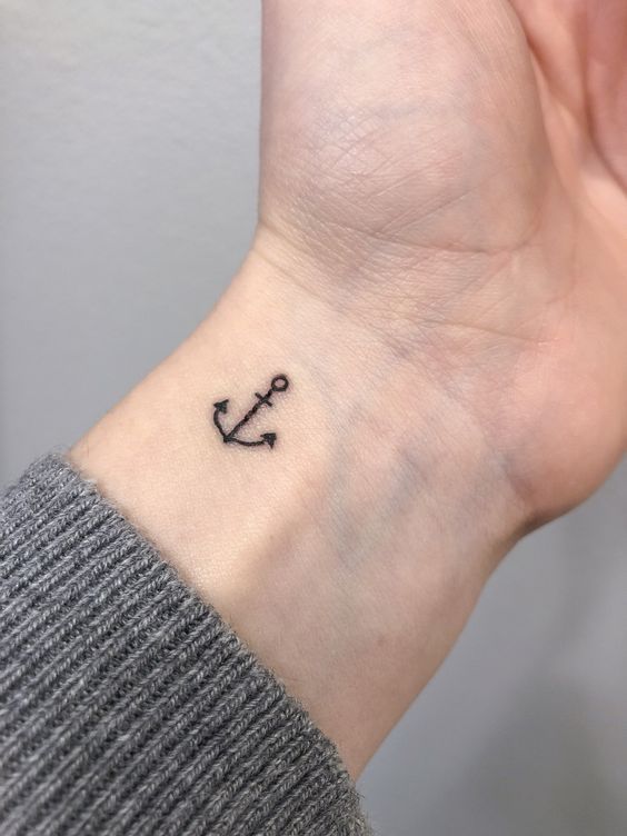 Small anchor wrist tattoo on a person's inner wrist, symbolizing stability and strength; minimalist design on light skin.