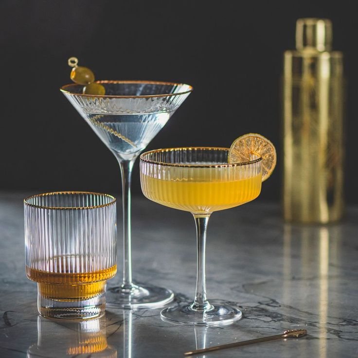 Stylish cocktails served in elegant glassware with a golden shaker in the background on a marble countertop.