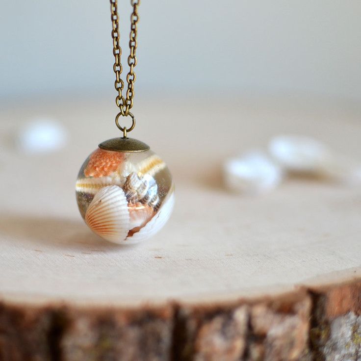 Elegant beach-themed pendant necklace featuring seashells encased in a round glass orb, resting on a wooden surface.