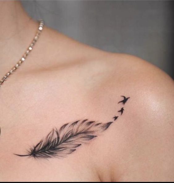 Minimalist feather tattoo with birds on collarbone. Delicate black ink design. Subtle, elegant body art.