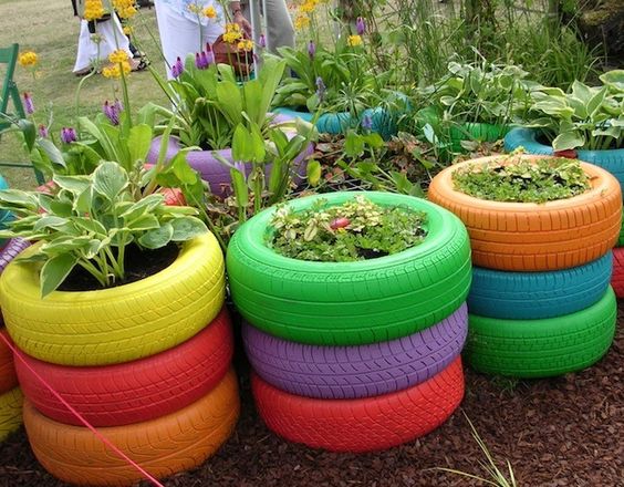 Colorful repurposed tire planters with green plants and flowers in a garden setting, promoting creative eco-friendly gardening.