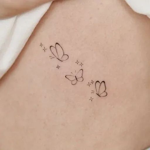 Minimalist butterfly tattoo design on skin, featuring three delicate butterflies with small star accents and fine linework.