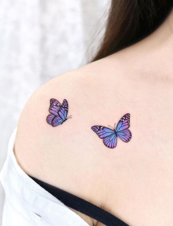 Two purple and blue butterfly tattoos on a person's shoulder, showcasing elegant and delicate body art.