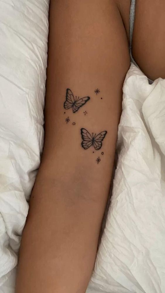 Leg tattoo of two butterflies surrounded by small stars and dots designed on inner thigh.