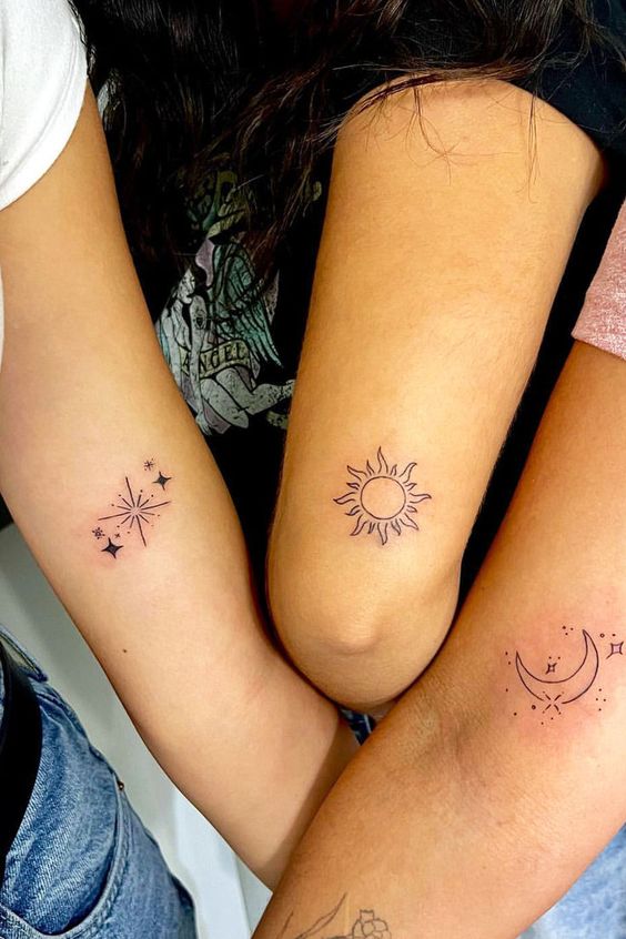 Three forearms with matching minimalist tattoos: a sun, stars, and a crescent moon, symbolizing celestial themes and friendship.