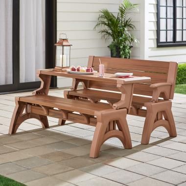 Outdoor patio setting with wooden convertible bench and table on tiled flooring, adorned with decor and lantern.